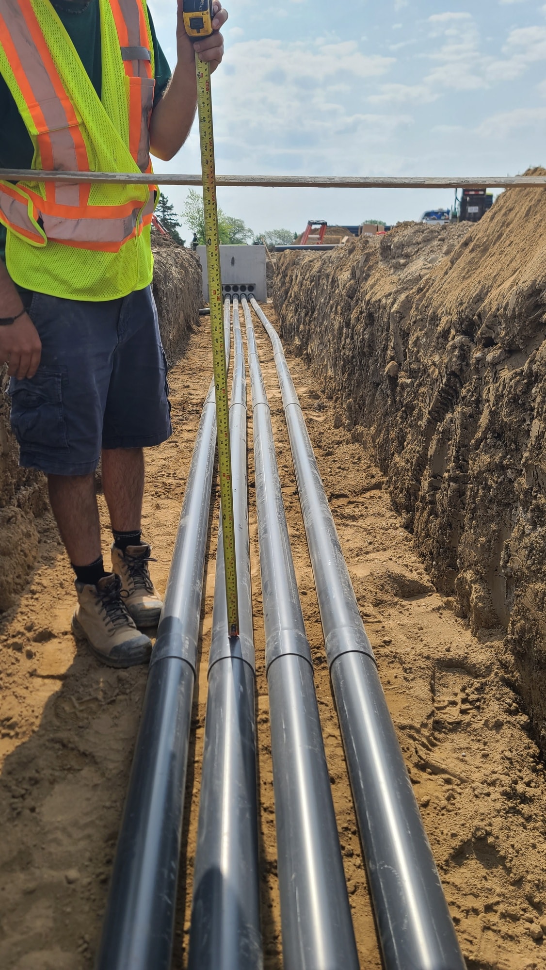 Construction worker measuring underground pipes in trench